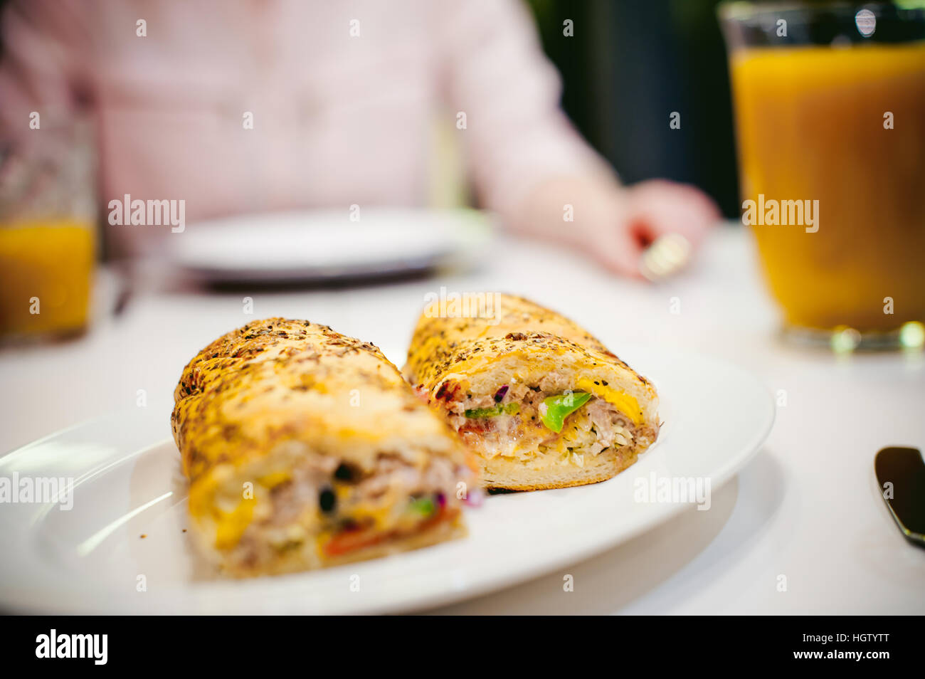 Très jolie jeune femme dans un chandail rose, manger à la maison. Le petit-déjeuner sandwich et jus de pêche. sur blanc tableau de l'intérieur lumineux de la cuisine dans la plaque est sable Banque D'Images