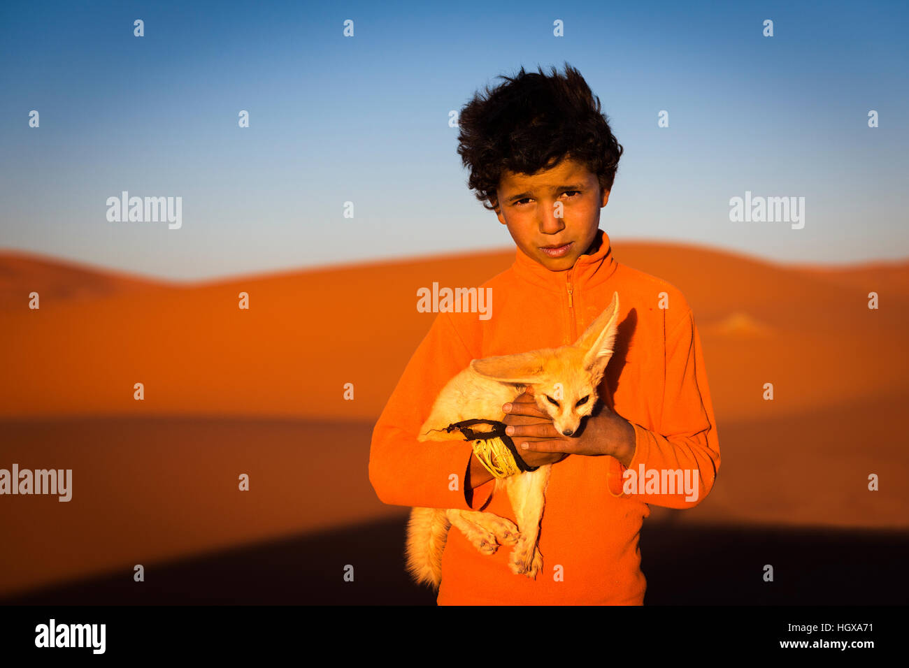 Merzouga, Maroc - 12 Avril 2016 : Berber enfant tenant un renard du désert pose dans les dunes de l'Erg Chebbi au Maroc. Banque D'Images