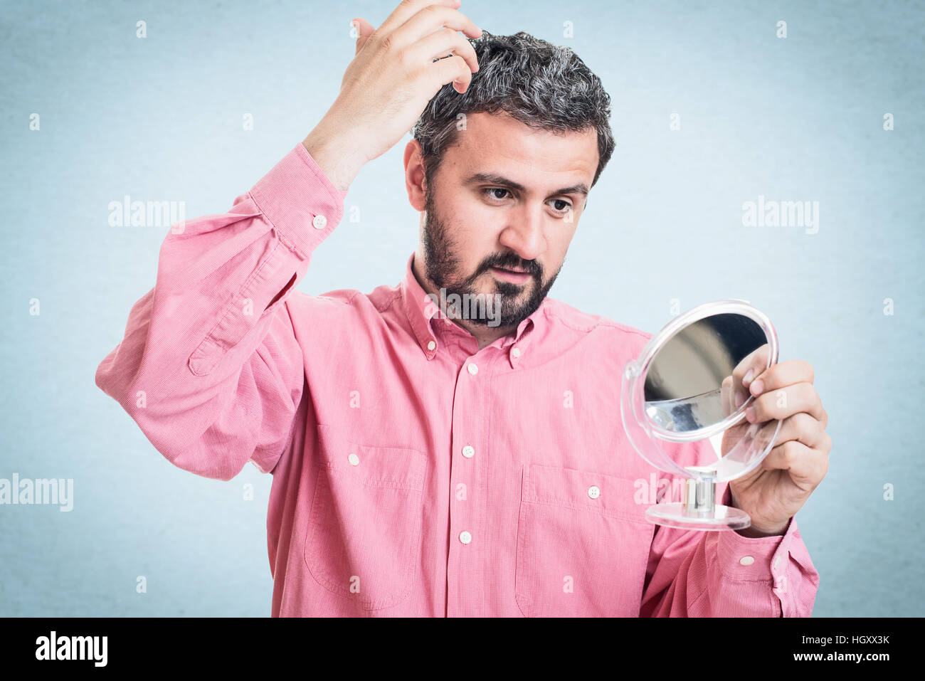 L'homme inquiet à propos de cheveux gris à la recherche dans un miroir Banque D'Images