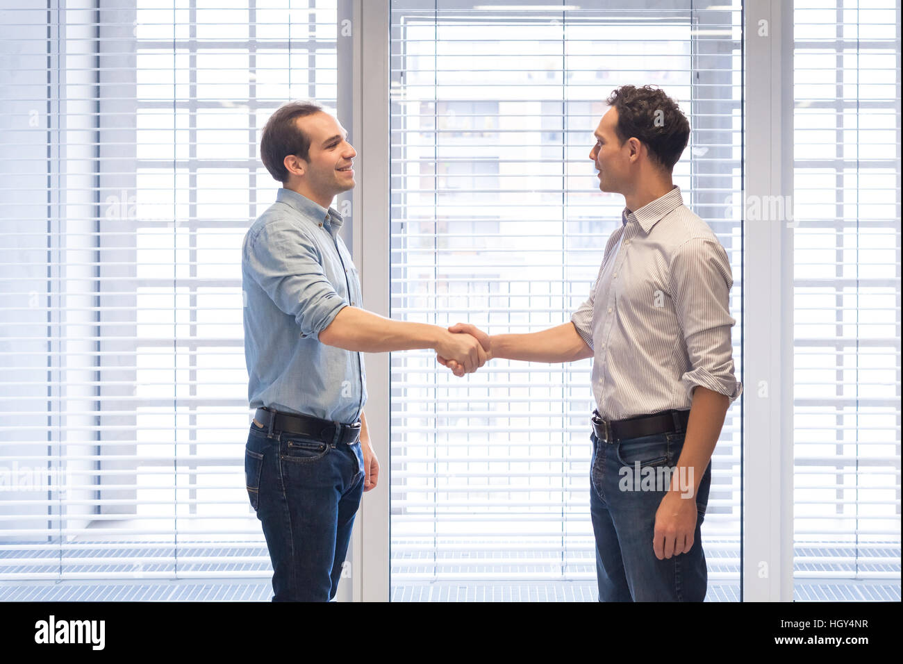 Deux collègues habillés de désinvolture shaking hands in a modern office interior comme un symbole d'accord Banque D'Images