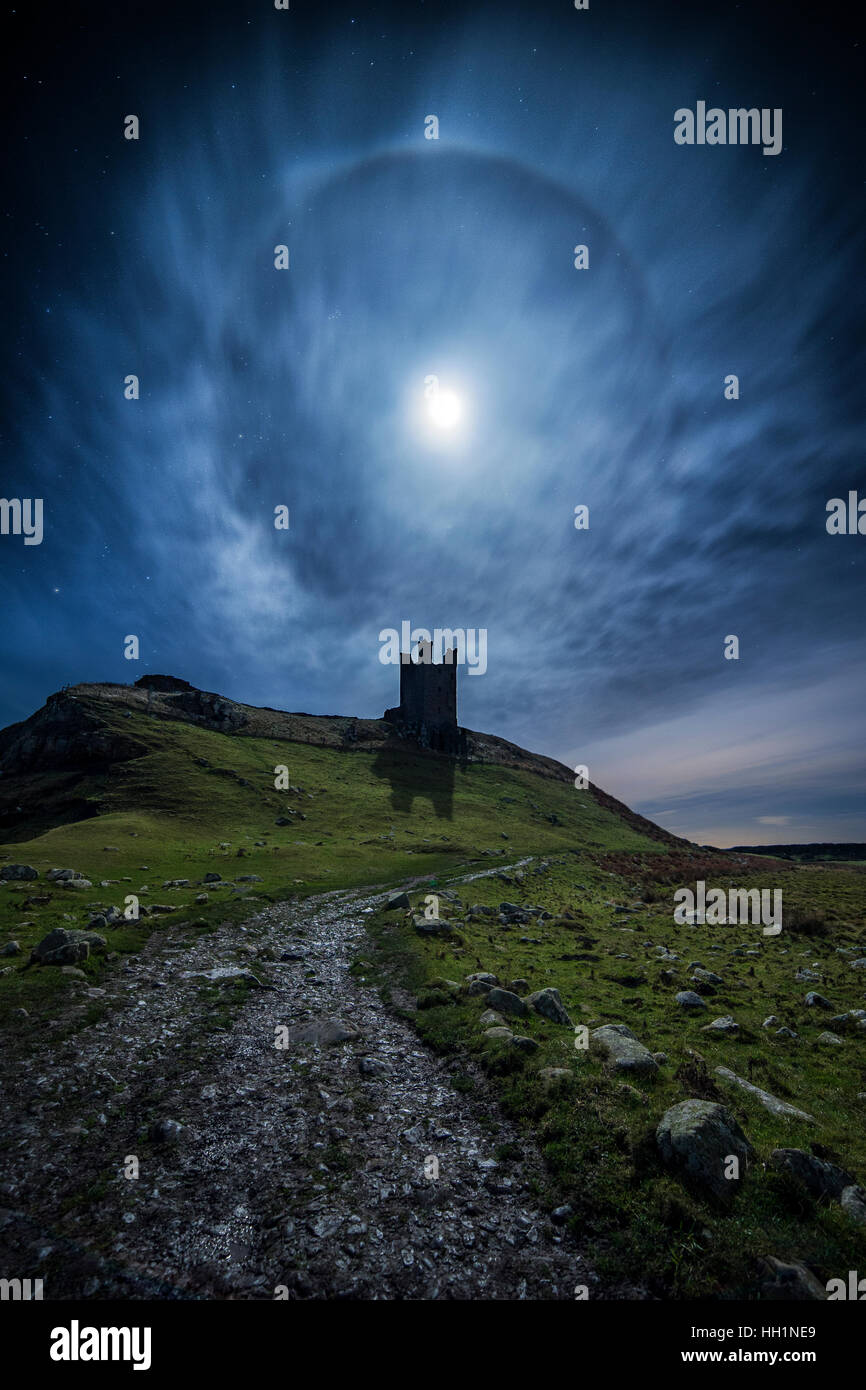 Un 22° Halo lunaire sur Château De Dunstanburgh sur la côte de Northumberland au Royaume-Uni Banque D'Images