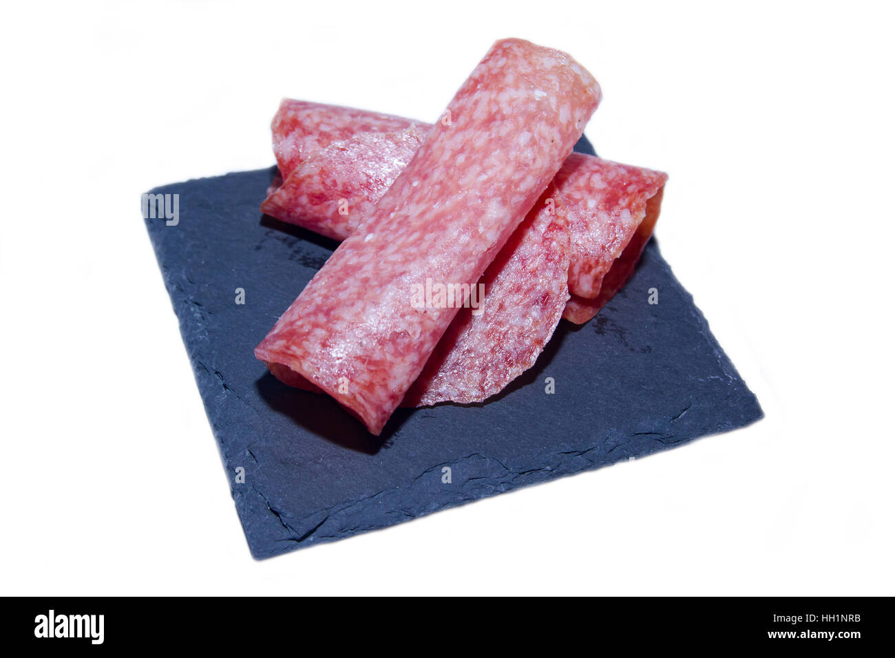 Tranches de salami sur une plaque en ardoise sur un fond blanc Banque D'Images