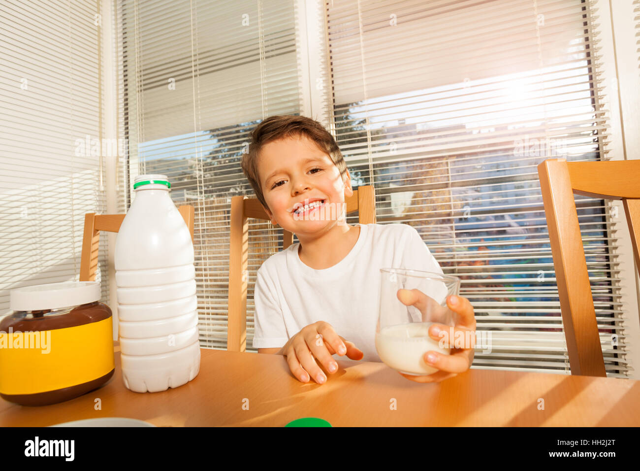 Happy boy holding glass avec du lait sitting at table Banque D'Images