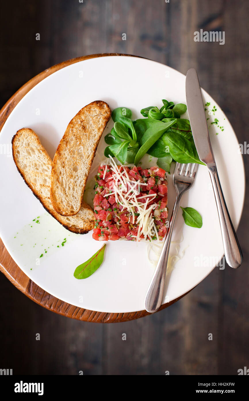 Tartare de boeuf aux épinards sur une assiette blanche. Isolé sur fond noir ou en bois foncé. Banque D'Images