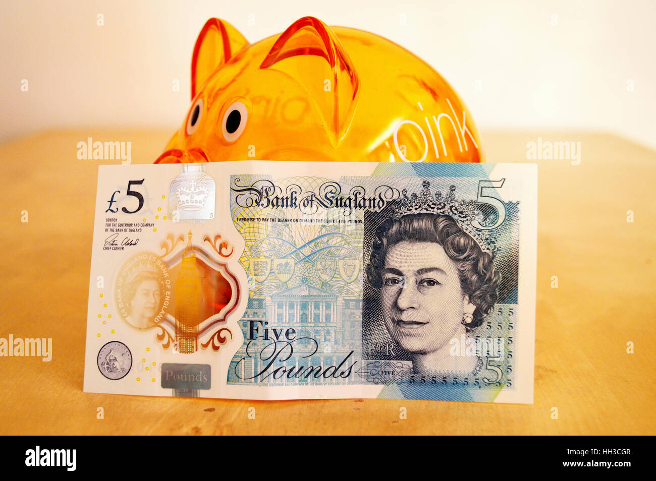 Avant de la polymère nouveau UK cinq livre appuyé contre une orange tirelire. Banque D'Images