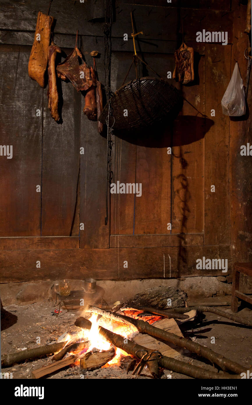 En plaques de viande suspendu au-dessus d'un feu de bois pour faire de la viande fumée dans le salon d'une ancienne ferme dans un village isolé dans les montagnes de l'ouest de la Chine. Banque D'Images
