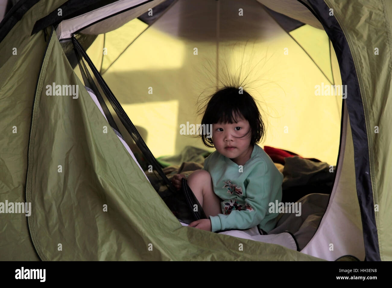 Une petite fille chinoise avec quelques cheveux en raison de l'électricité statique joue dans une tente pendant un voyage de camping familial en Chine. Banque D'Images