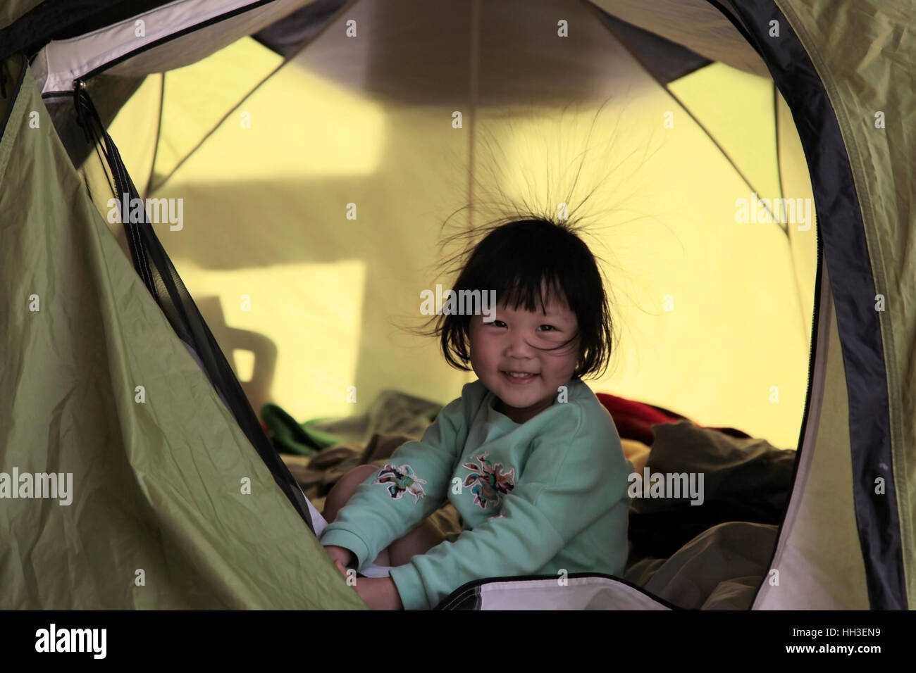 Une petite fille chinoise avec quelques cheveux en raison de l'électricité statique joue dans une tente pendant un voyage de camping familial en Chine. Banque D'Images