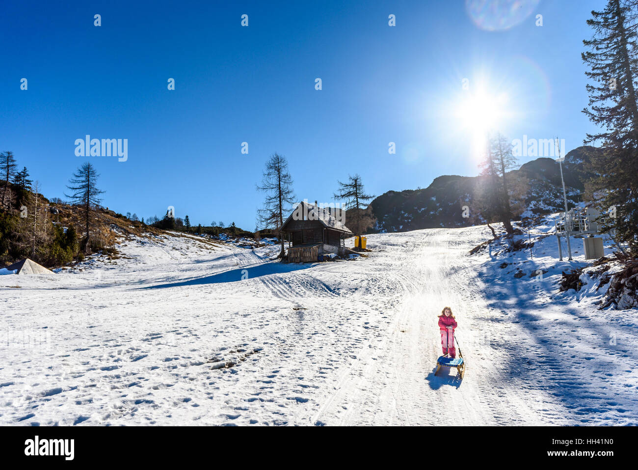 Fille tire-luges de ski de porter des vêtements d'hiver. Station de ski de haute montagne, vacances, maison de vacances journée ensoleillée et des pics de montagne. Banque D'Images