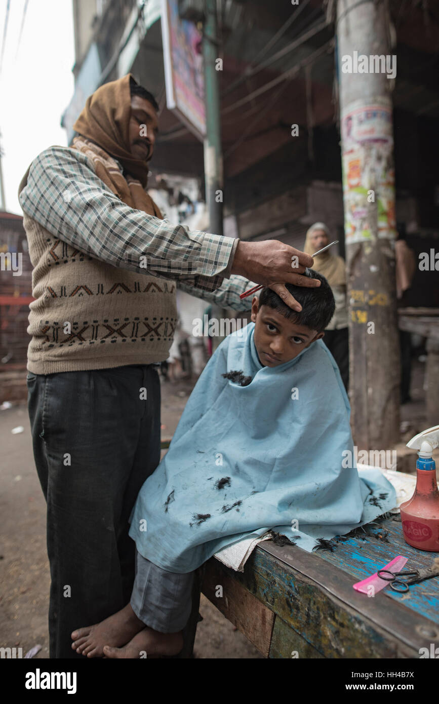 Un Indien coiffure donne une coupe de cheveux d'un jeune garçon sur un début de l'hiver matin à son côté route de fortune, d'un salon de coiffure. Banque D'Images