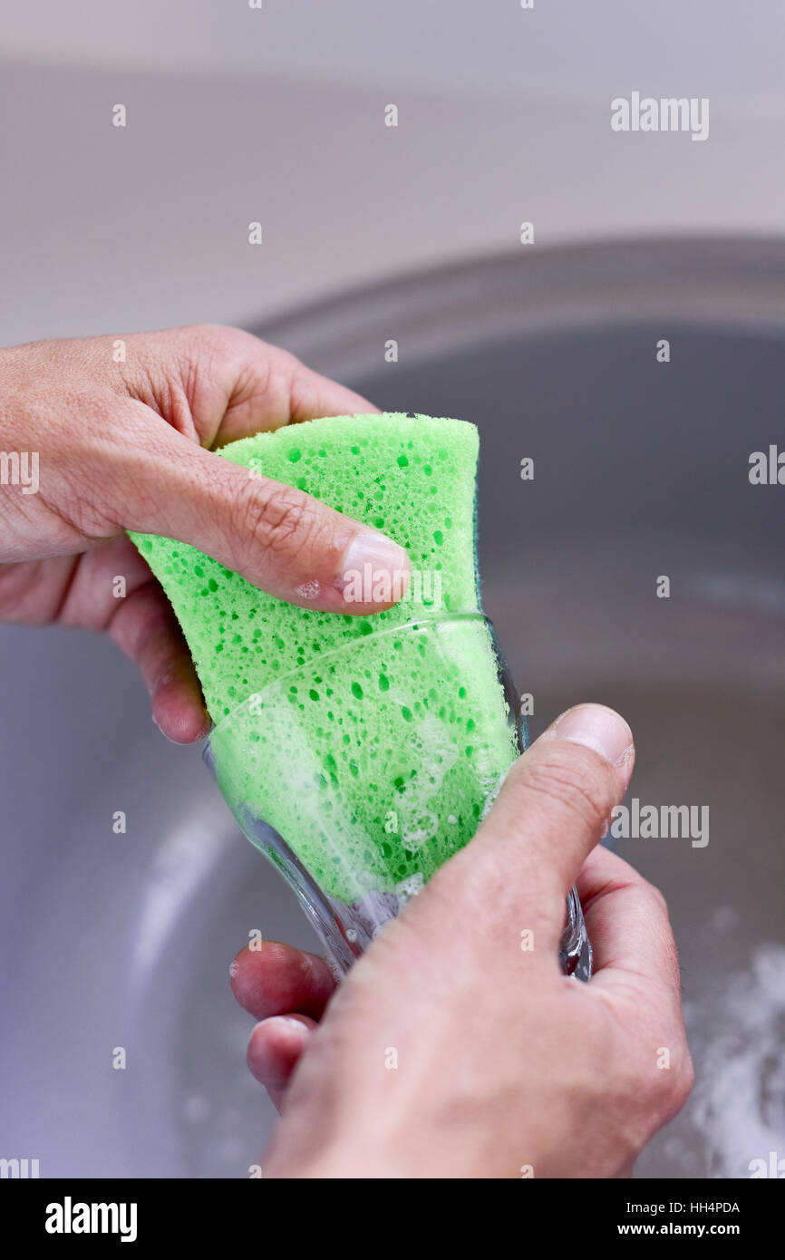 Libre d'un jeune homme lave un verre dans un évier de cuisine avec une éponge verte Banque D'Images