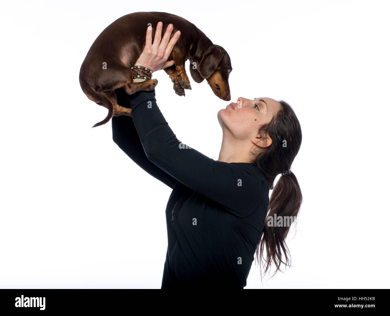 Caucasian brunette tient son chien teckel dans l'air ce qui lui donne un baiser Banque D'Images