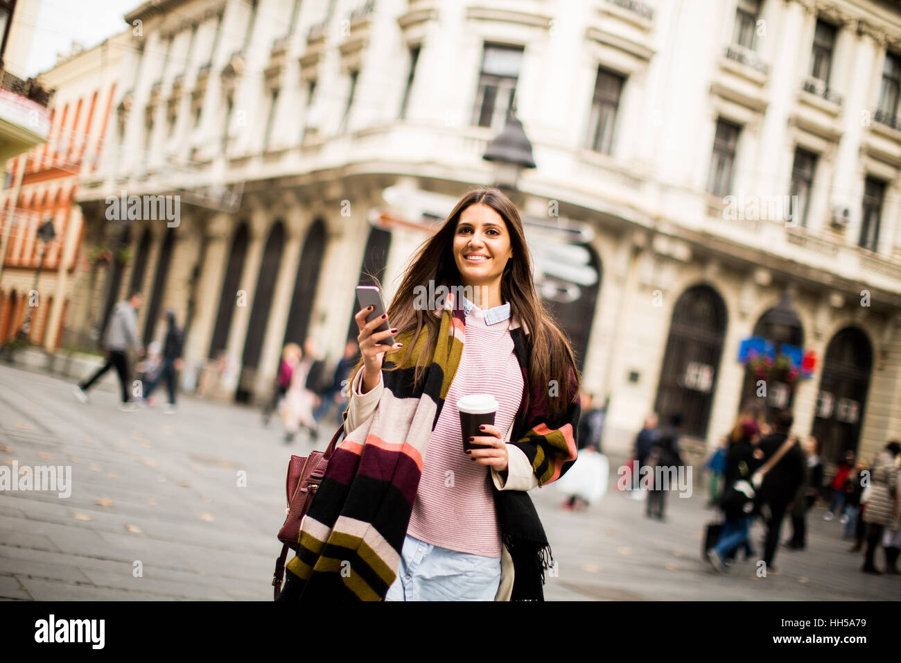 Jeune femme avec du café pour aller et le téléphone mobile dans la main dans la rue Banque D'Images