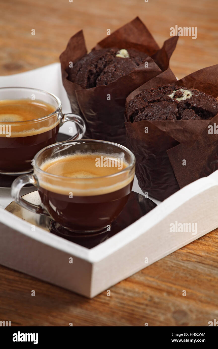 Photo de deux muffins de chocolat et deux tasses de café espresso ou café reposant sur un bac blanc au service de profondeur de champ à l'accent au milieu Banque D'Images