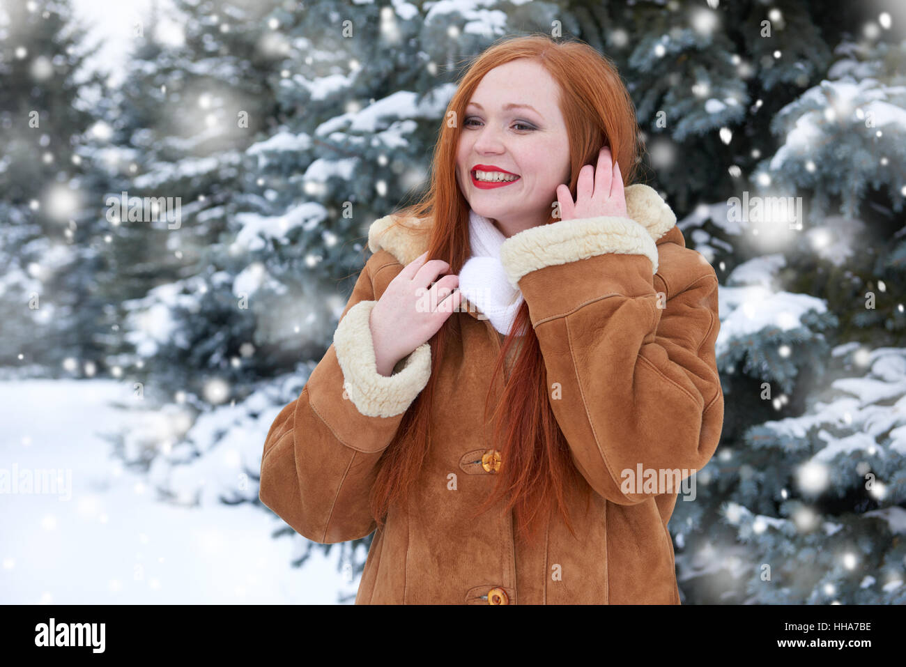 Belle femme pour profiter de l'hiver, la neige sur les sapins en forêt, longs cheveux rouges, portant un manteau en peau de mouton Banque D'Images