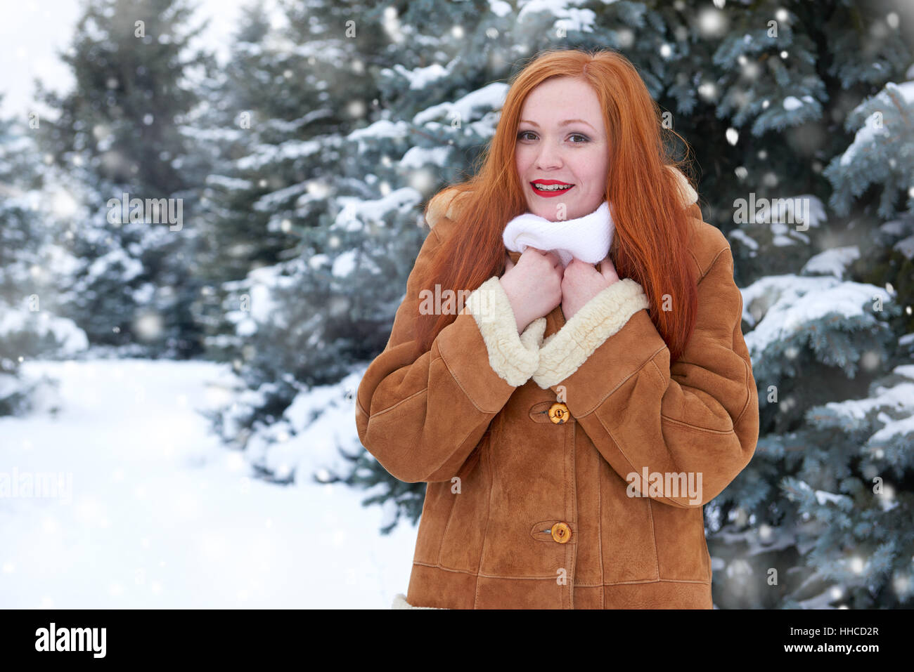 Belle femme pour profiter de l'hiver, la neige sur les sapins en forêt, longs cheveux rouges, portant un manteau en peau de mouton Banque D'Images