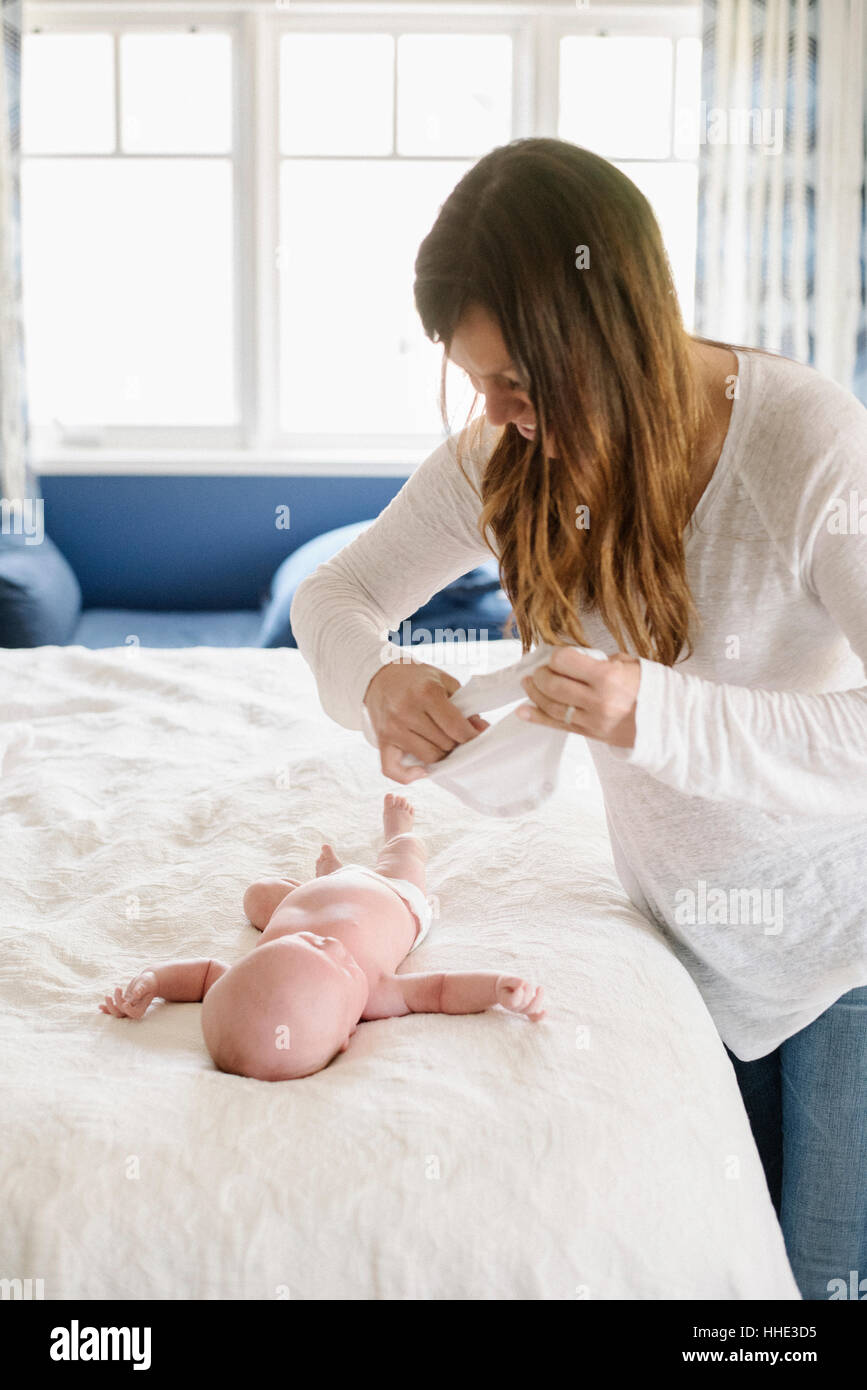 Une mère s'habiller son bébé sur un lit. Banque D'Images