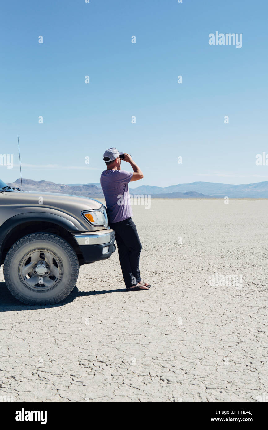 Homme debout sur le vaste désert, regardant à travers des jumelles et appuyé contre un camion, Black Rock Desert Banque D'Images