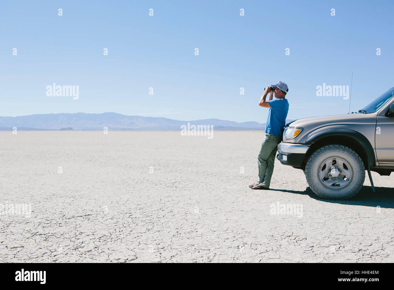 Homme debout sur le vaste désert, regardant à travers des jumelles et appuyé contre un camion, Black Rock Desert Banque D'Images