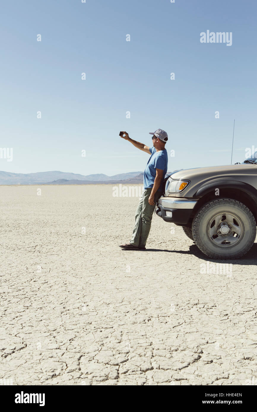 Laissant l'homme à l'encontre de chariot en désert, à l'aide de smart phone, Black Rock Desert, Nevada Banque D'Images