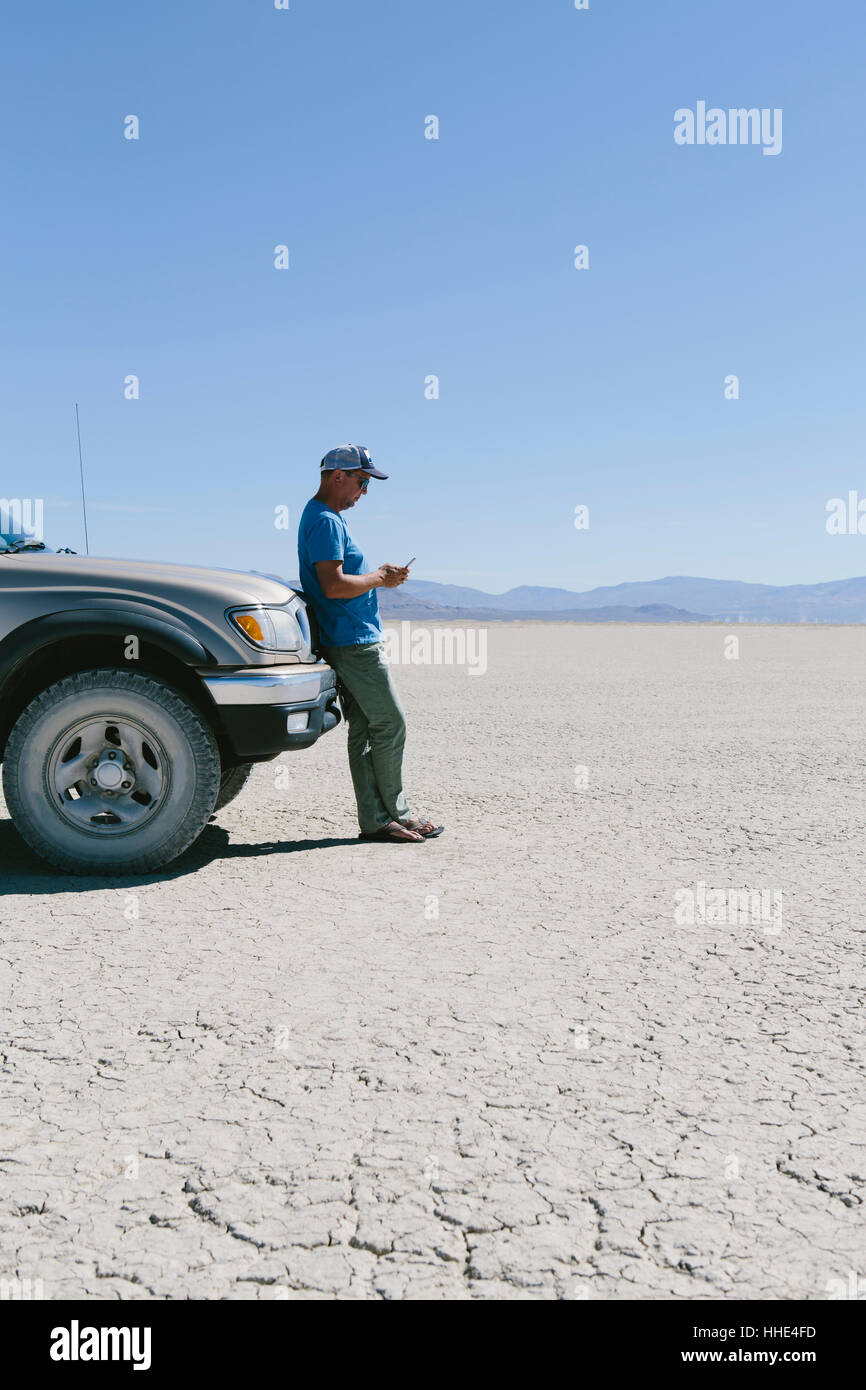 Laissant l'homme à l'encontre de chariot en désert, à l'aide de smart phone, Black Rock Desert, Nevada Banque D'Images