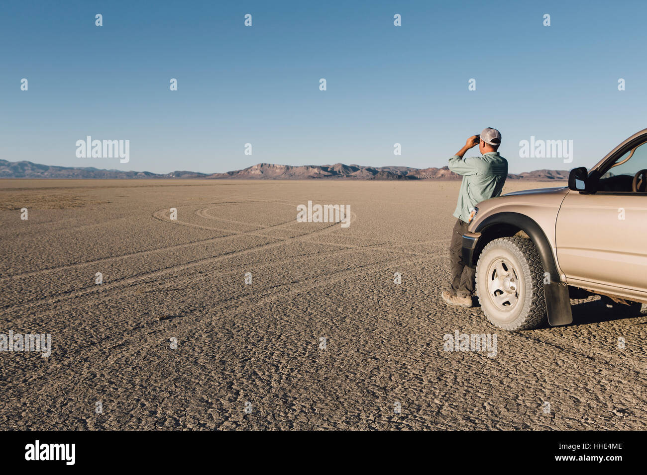 Homme debout sur le vaste désert, regardant à travers des jumelles et appuyé contre un camion, Black Rock Desert Banque D'Images