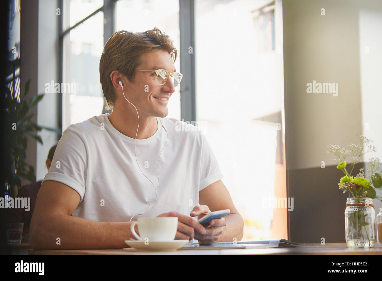 L'homme souriant avec des écouteurs et un lecteur mp3, à écouter de la musique de boire du café en café Banque D'Images