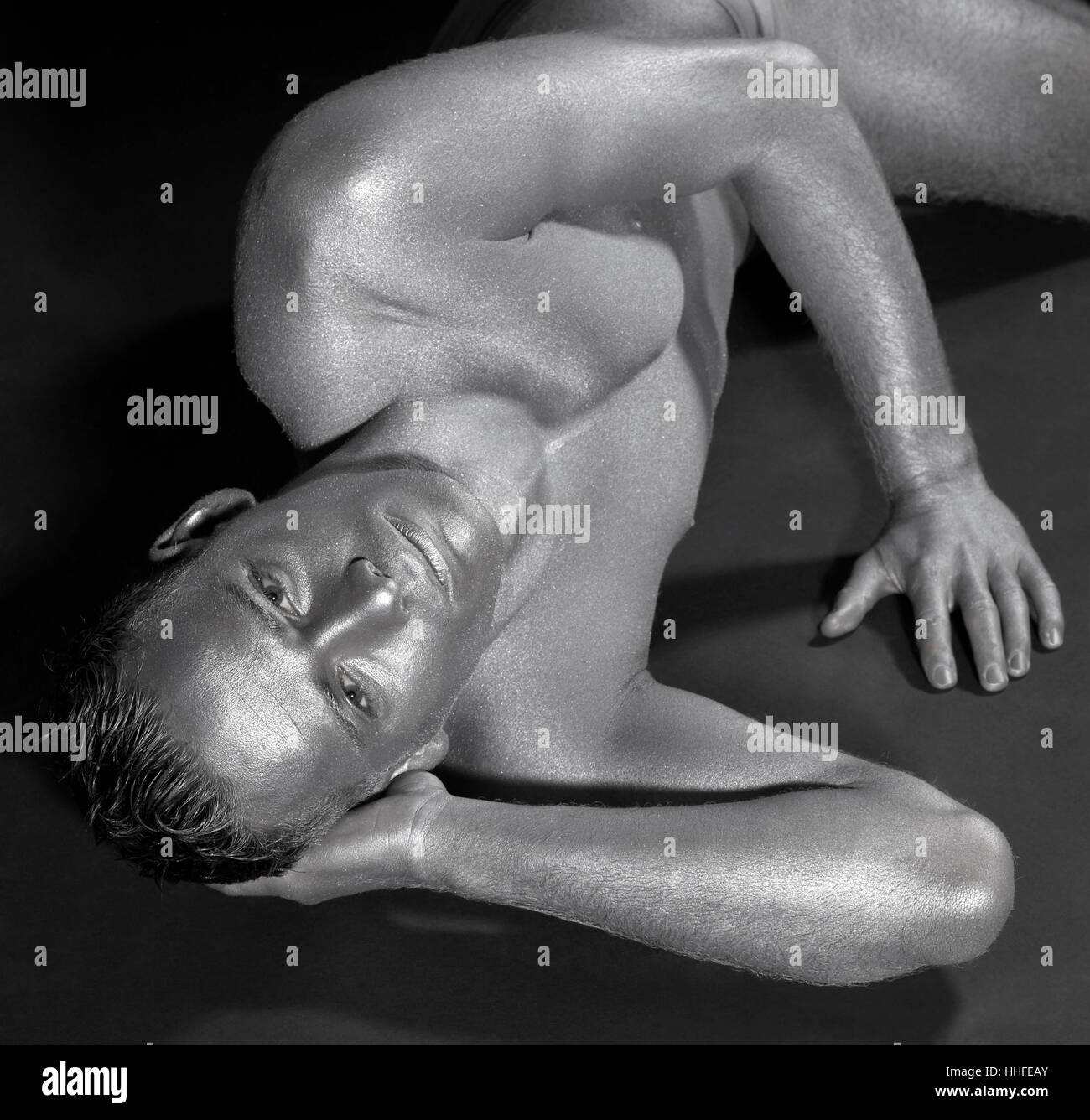 La photographie de studio d'un homme bodypainted d'argent alors qu'elle repose sur la masse sombre Banque D'Images