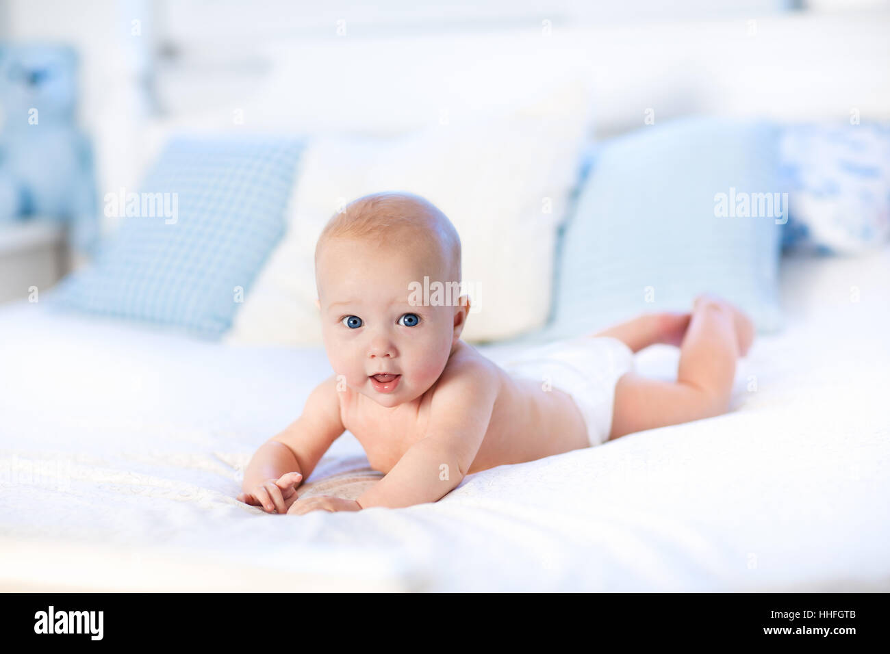 Bébé garçon vêtu de blanc à couches chambre ensoleillée. Le nouveau-né de se détendre dans le lit. Garderie pour les enfants. Textile et de la literie pour enfant Banque D'Images