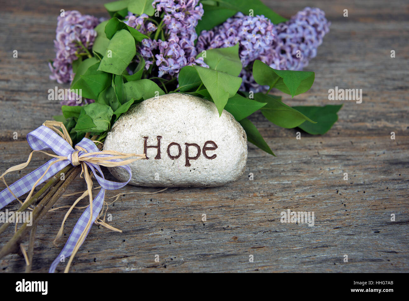 Mot espoir sculpté dans la pierre avec bouquet de lilas sur bois rustique Banque D'Images