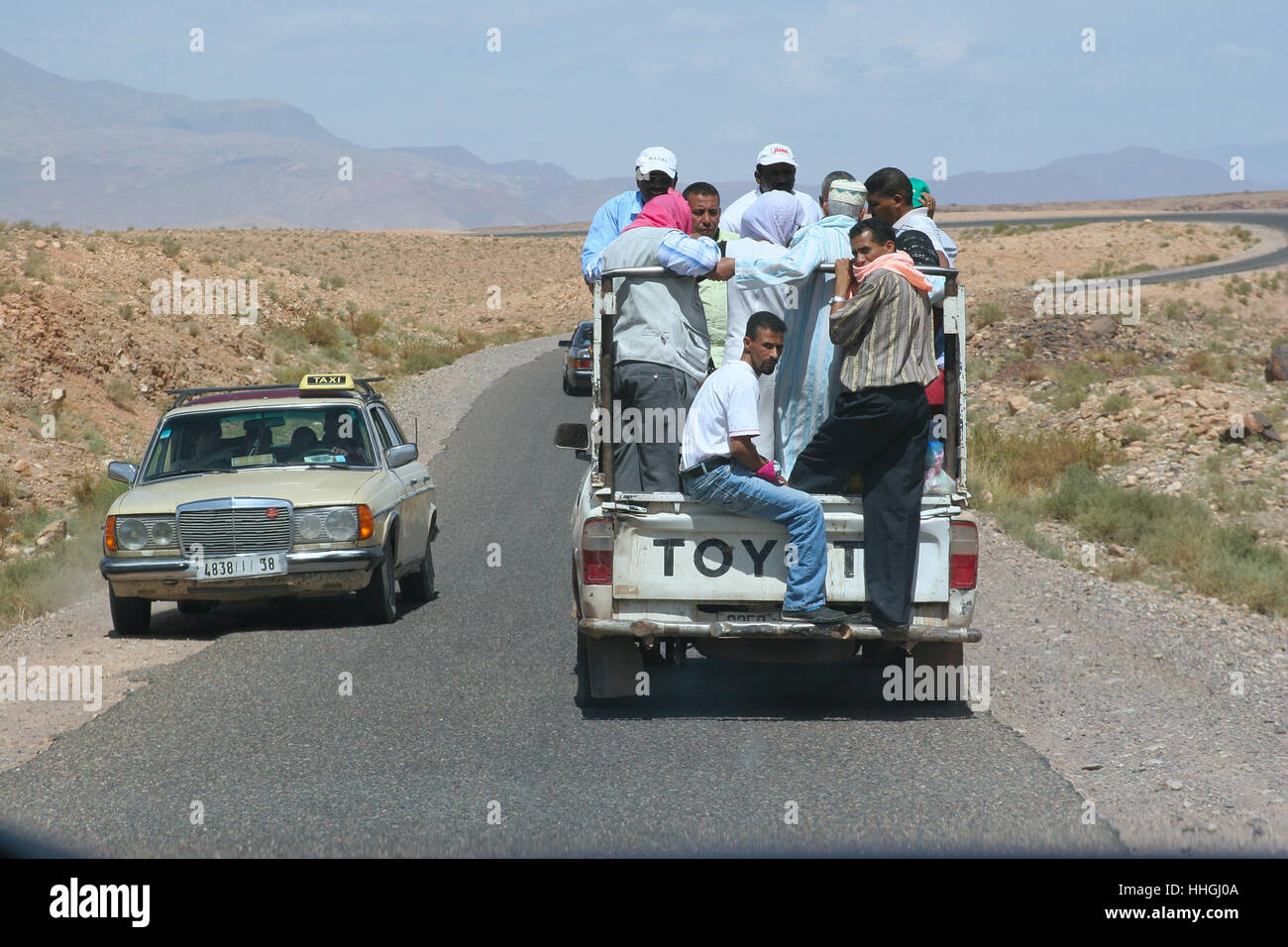 Vieux taxi Mercedes laissant place à un pick-up surchargé sur une route marocaine Banque D'Images