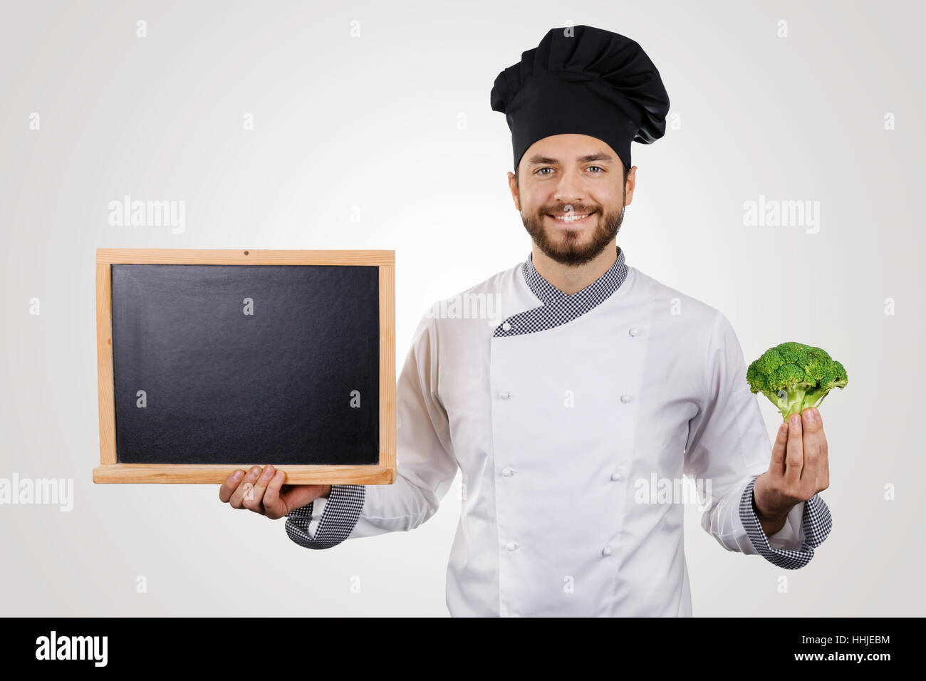 Souriante jeune chef avec tableau noir en blanc et le brocoli dans la main Banque D'Images