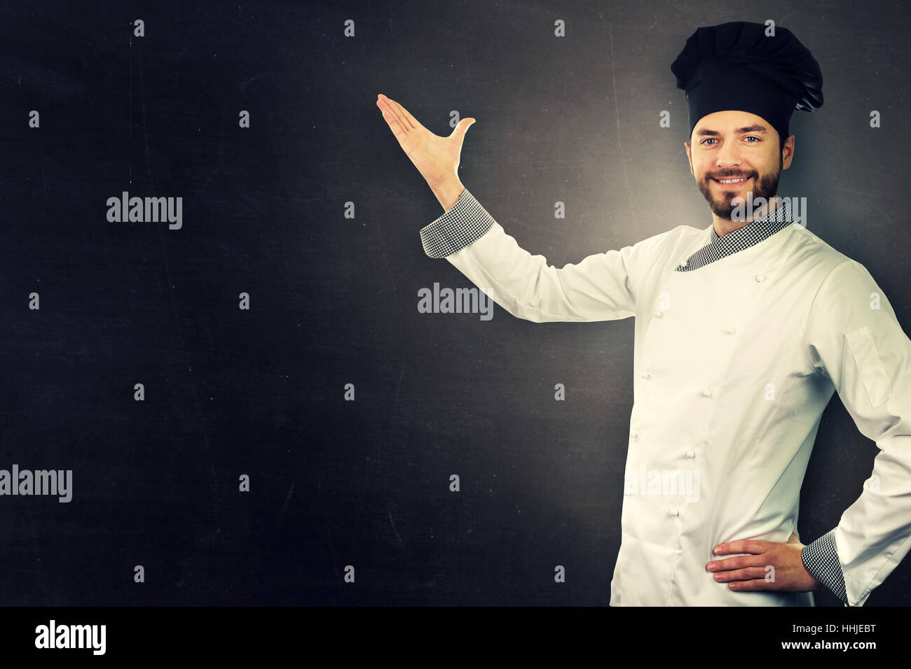 Young smiling chef en uniforme blanc sur noir with copy space Banque D'Images