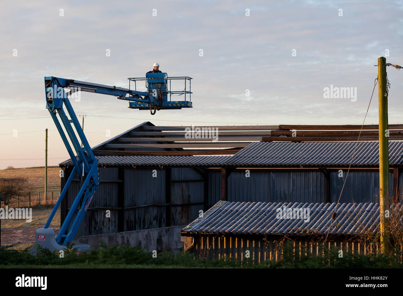 Travailleur de la construction avec un casque et gilet de relevage hydraulique fonctionne pour réparer le toit grange Kent, UK Banque D'Images