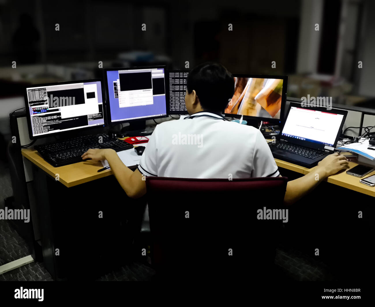 Asian male ingénieur réseau travaillant sur plusieurs moniteurs avec une main sur le clavier tandis que l'autre sur la souris de bureau bureau Banque D'Images
