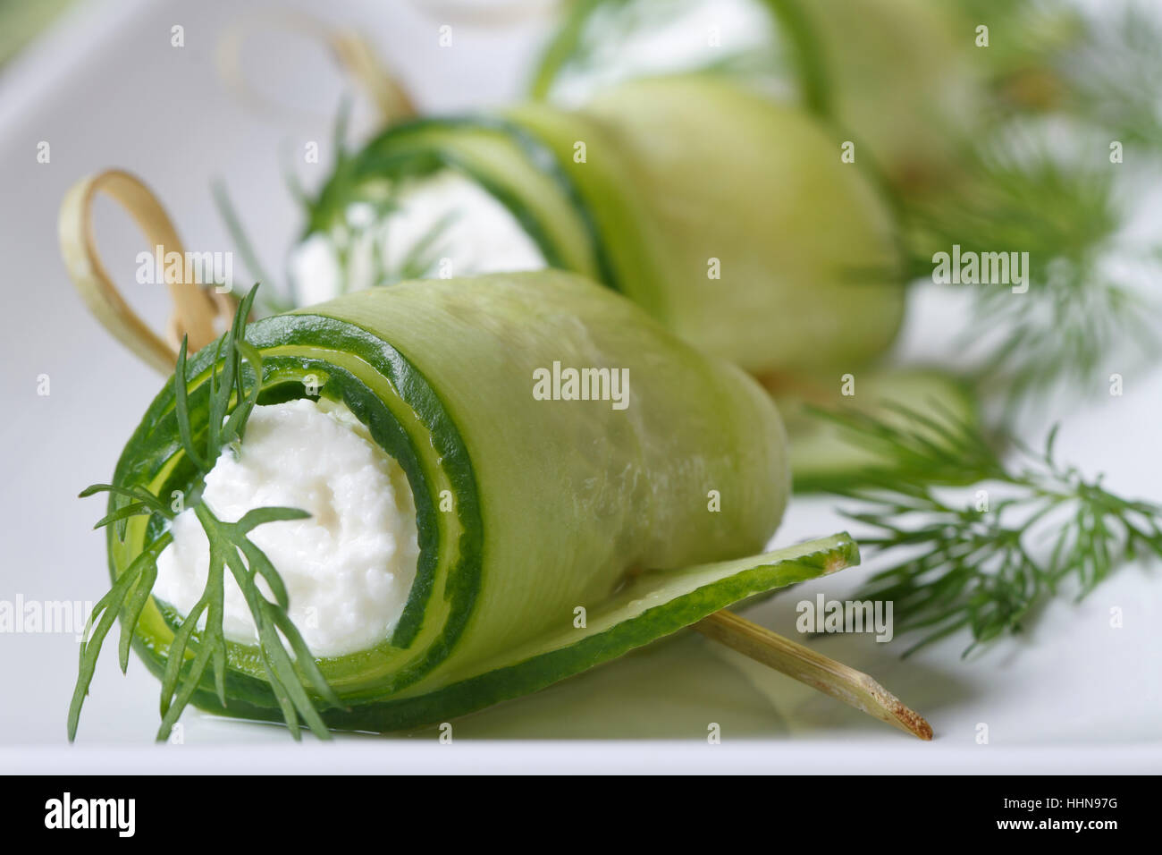 Rouleaux de concombre avec du fromage et de l'aneth gros plan sur une assiette blanche horizontale. Banque D'Images