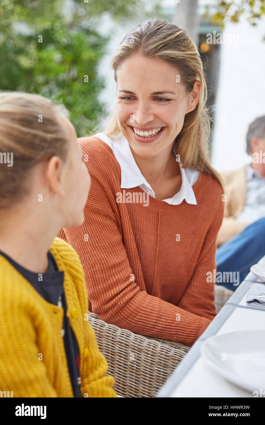 Smiling mother and daughter talking at table patio Banque D'Images