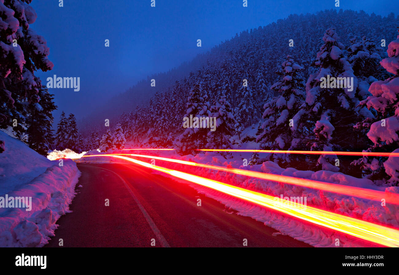 Des sentiers de lumière rouge par une voiture, dans une route dans une région montagneuse de la Grèce, au sein d'une forêt de sapins pleine de neige, en hiver de 2017. Banque D'Images