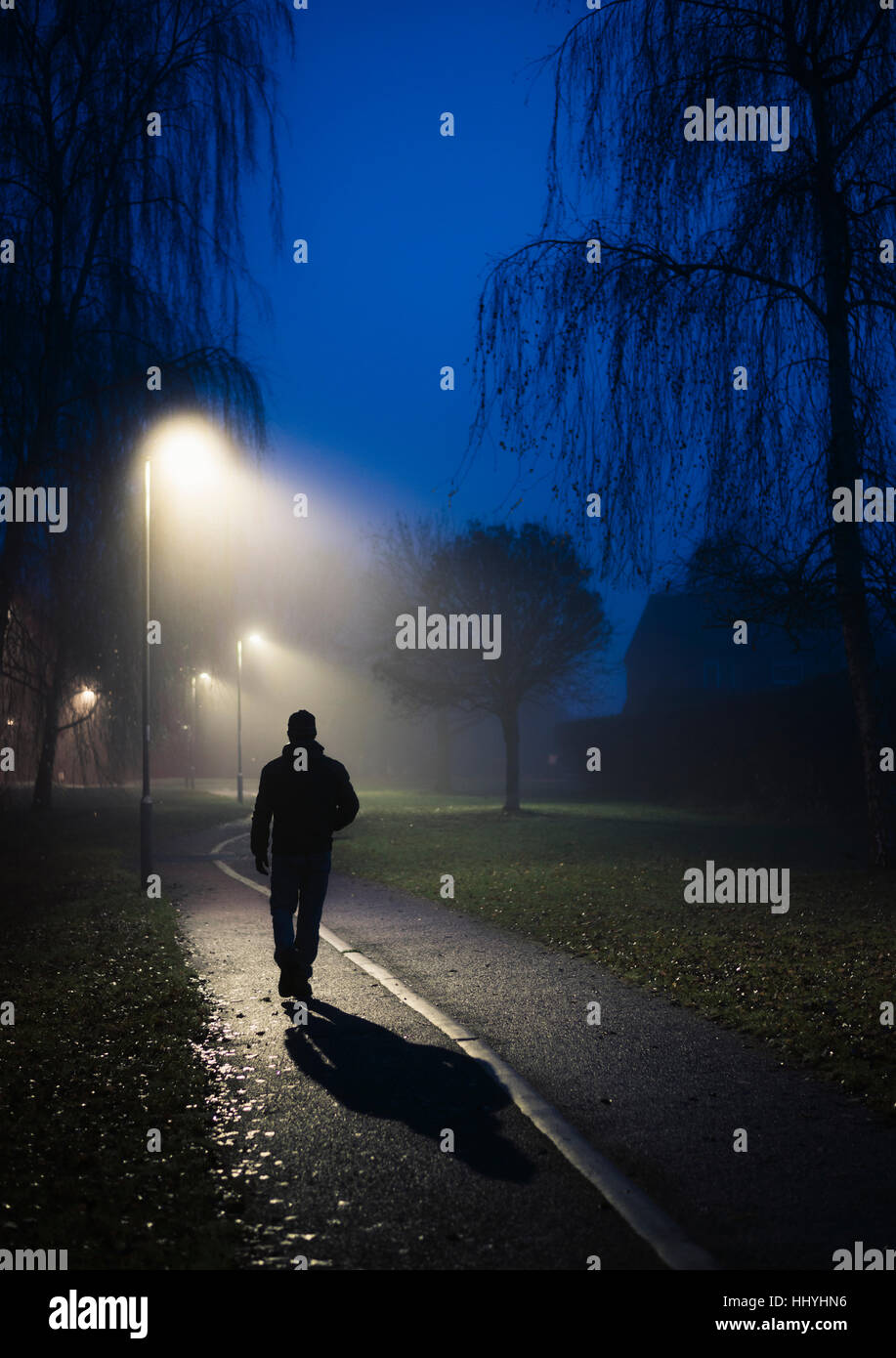 Une figure solitaire marchant le long d'un chemin éclairé par des lampadaires Banque D'Images
