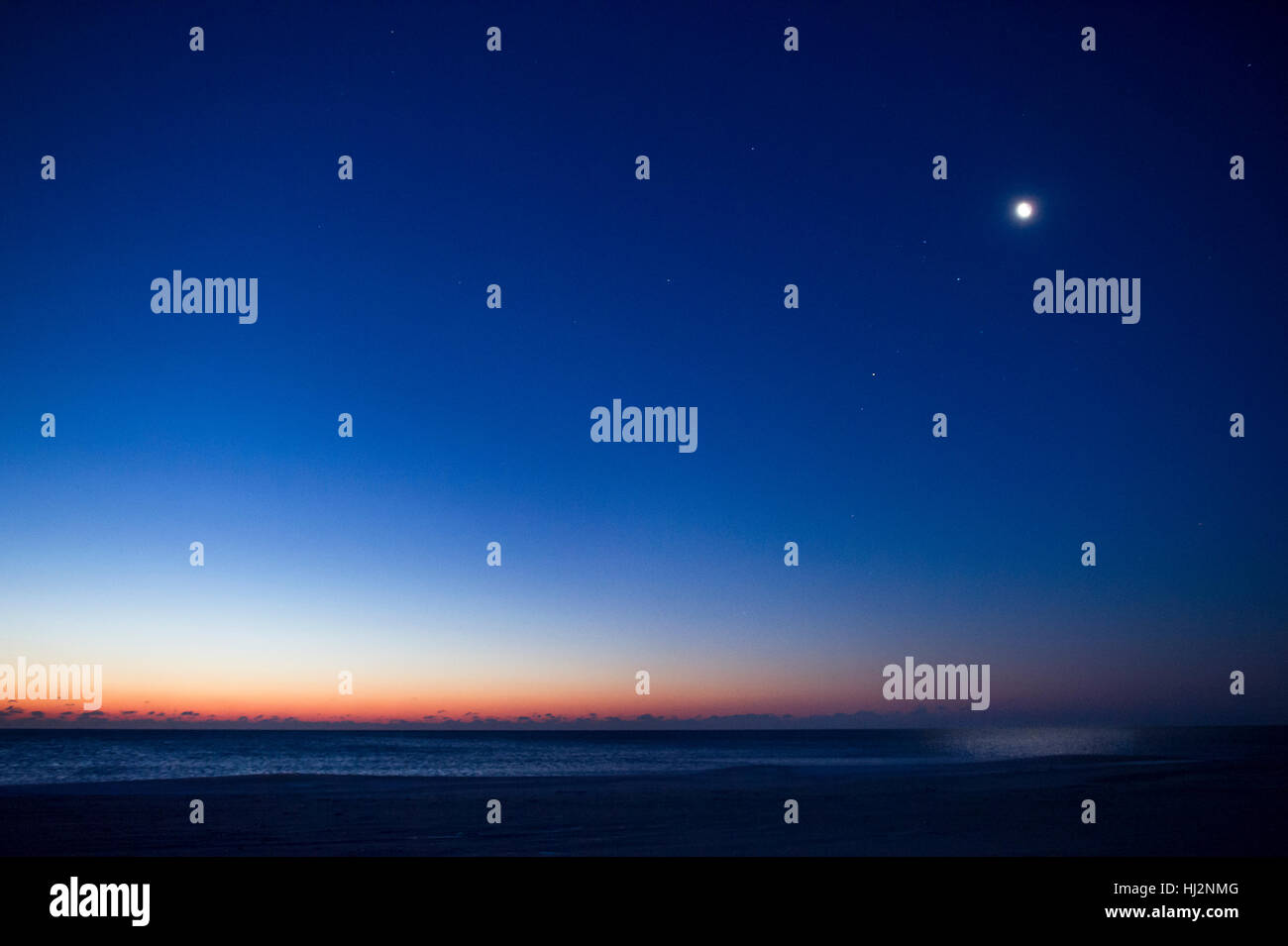 La lune et les étoiles sont encore visibles comme le soleil commence à s'allumer l'horizon sur l'Océan Atlantique sur une plage. Banque D'Images