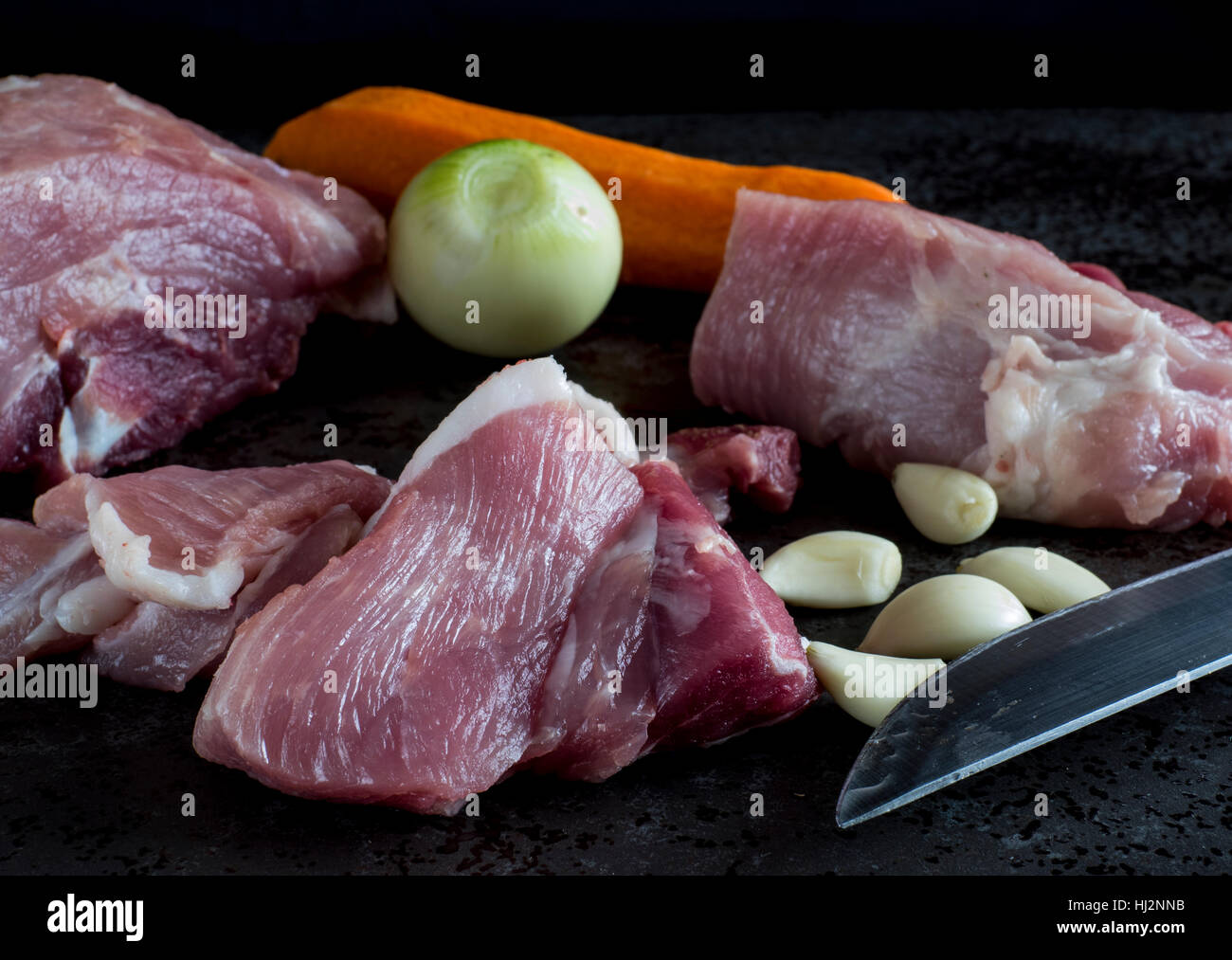 Commune de matières premières de viande de porc, oignon, ail et carotte au fond de la pierre sombre Banque D'Images