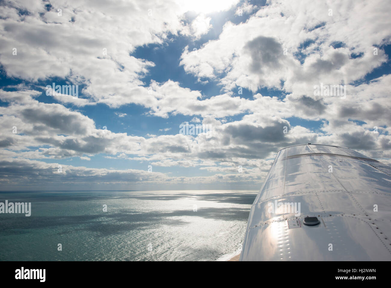 Vue d'un petit avion survolant l'océan le long d'une côte avec puffy nuages blancs dans un ciel bleu. Banque D'Images