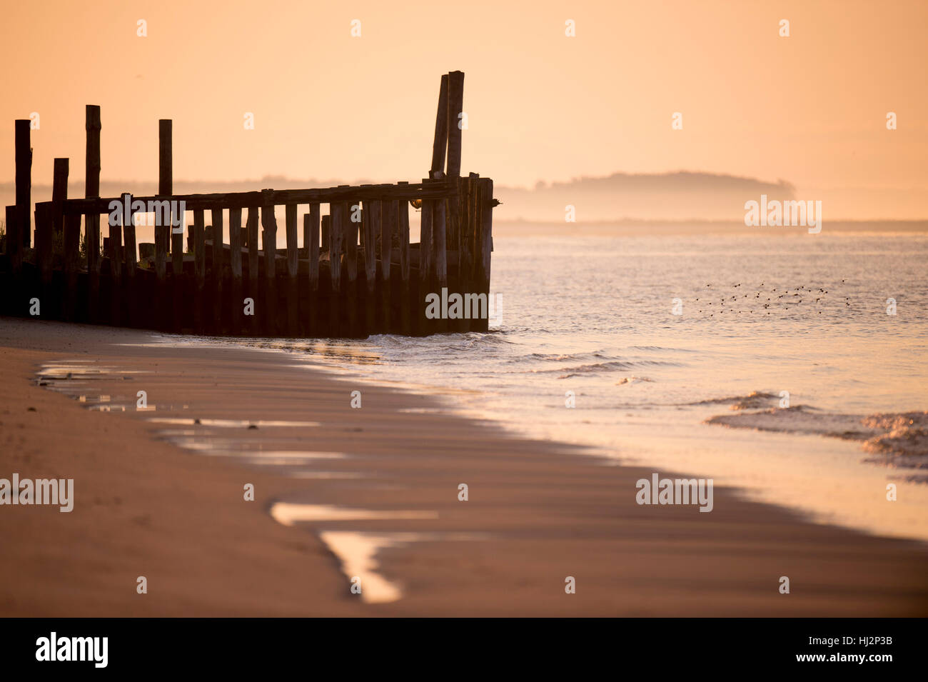 Un vieux quai qui s'effondre sur une plage de sable fin au lever du soleil. Banque D'Images