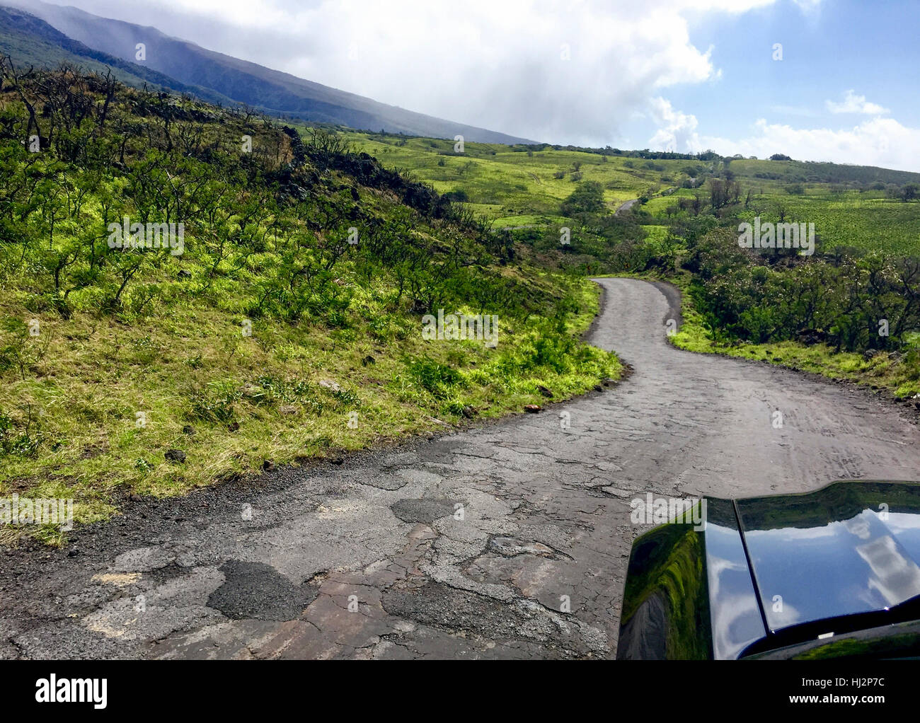 À peu près une route pavée à travers une montagne verte avec une voiture noire au premier plan. Banque D'Images