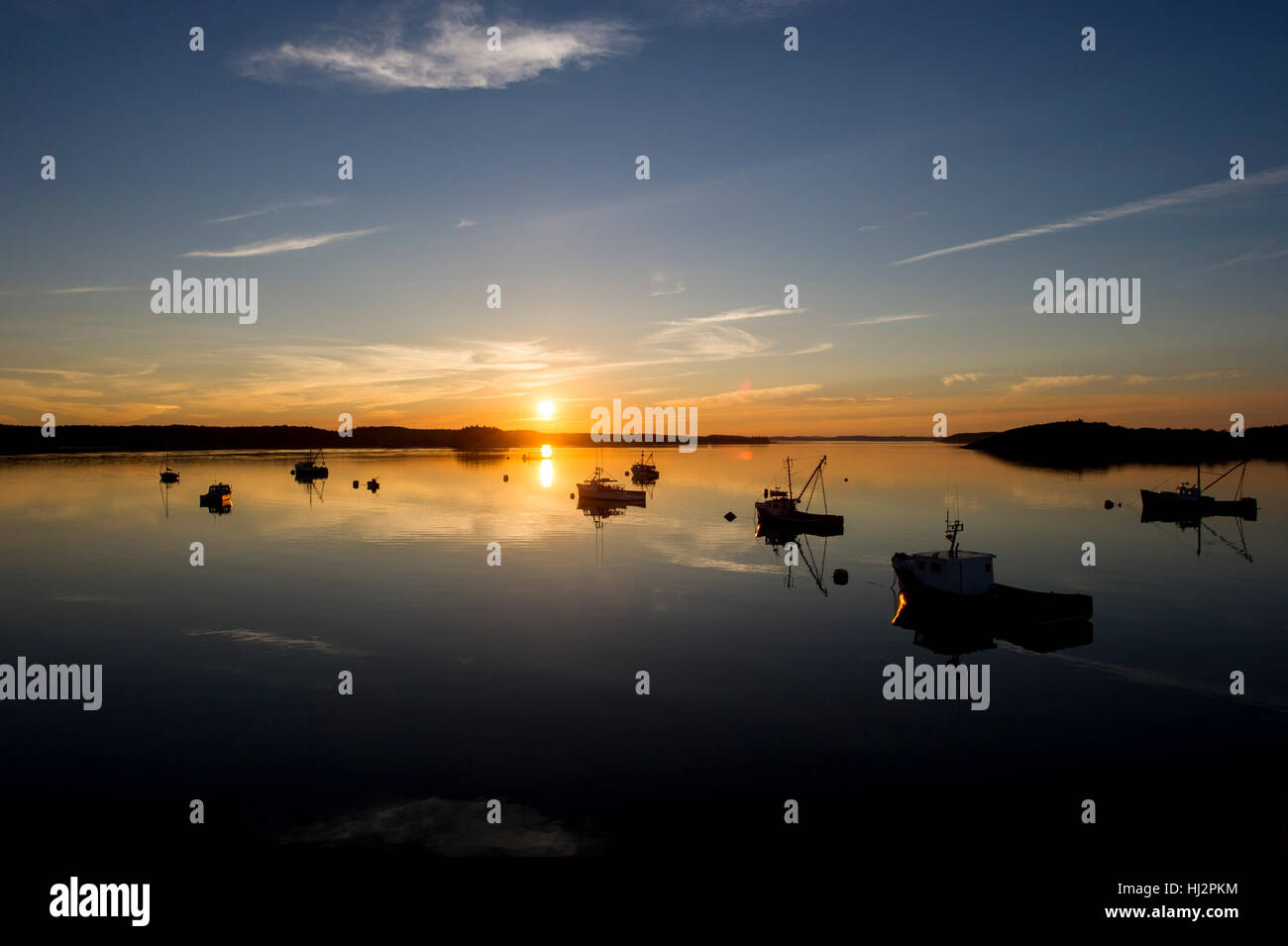 Le soleil se couche sur un port calme avec de nombreux bateaux de pêche ancrés. Banque D'Images