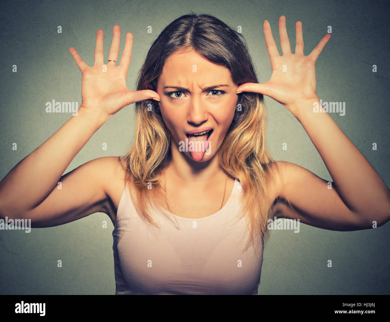 Jolie jeune femme avec drôle de visage se moquer de quelqu'un coller sa langue dehors isolé sur fond de mur gris Banque D'Images