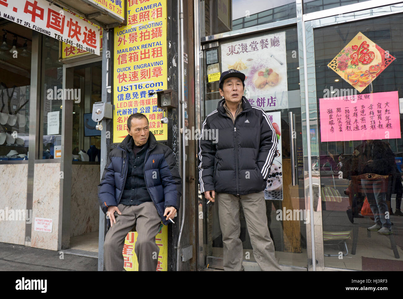 Deux Chinois travailleurs américains à l'extérieur sur une pause fumeurs sur Main Street dans le quartier chinois, le rinçage, Queens, New York. Banque D'Images