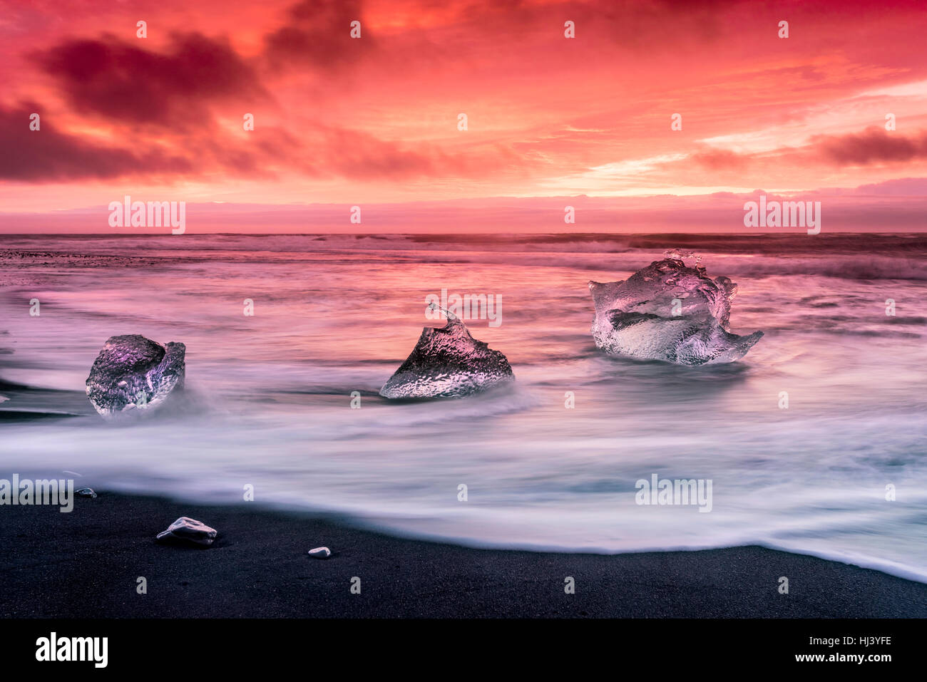 Un iceberg le long de la rive du Jokulsarlon glacial lagoon lors d'un rouge vibrant sunrise repose immobile comme il est entouré par l'eau de mer froide. Banque D'Images