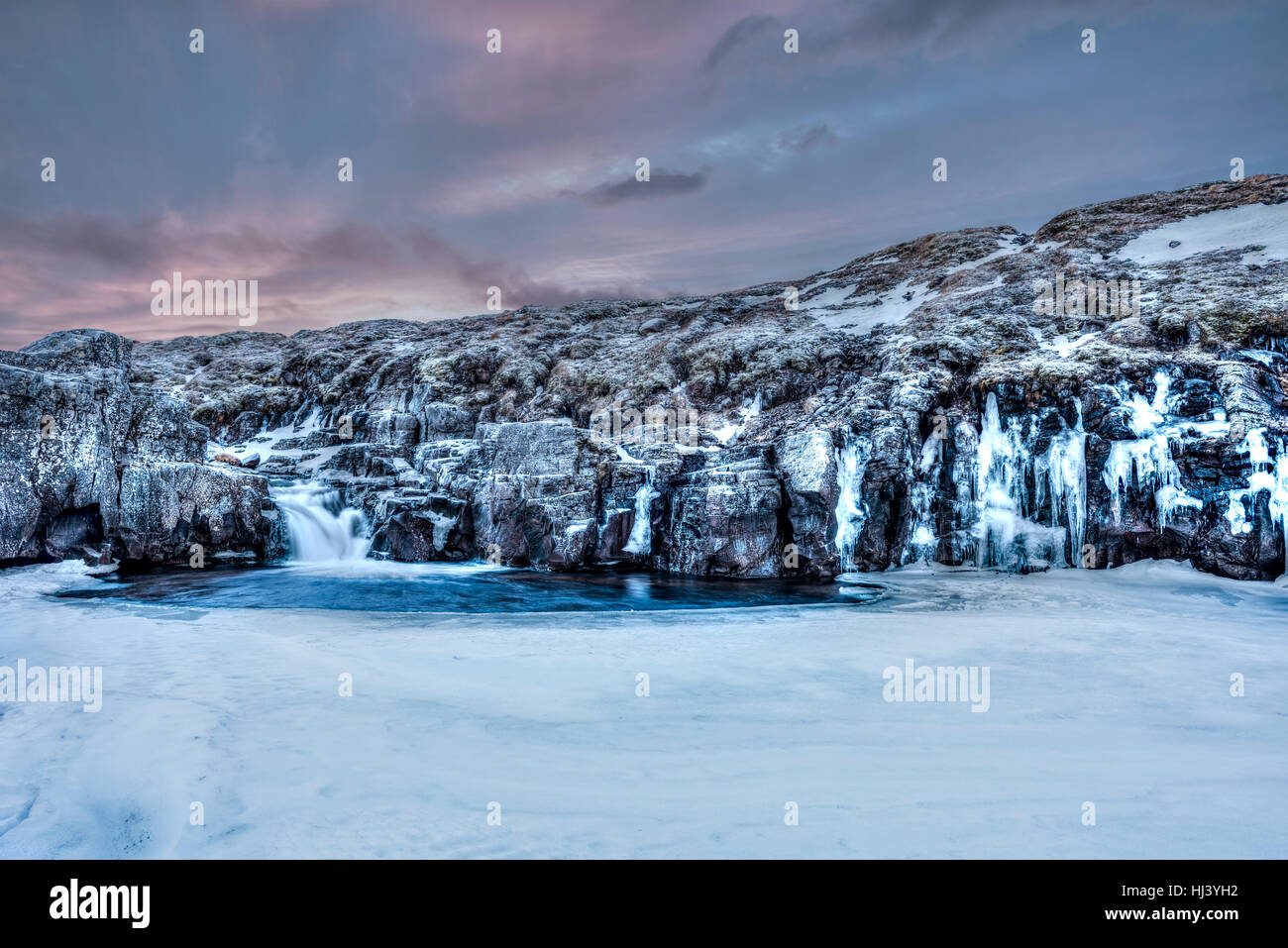 Une rivière gelée dans les hautes terres d'Islande encadrée par un ciel pastel foncé et le terrain accidenté offre des paysages pittoresques illustrant le désert gelé. Banque D'Images