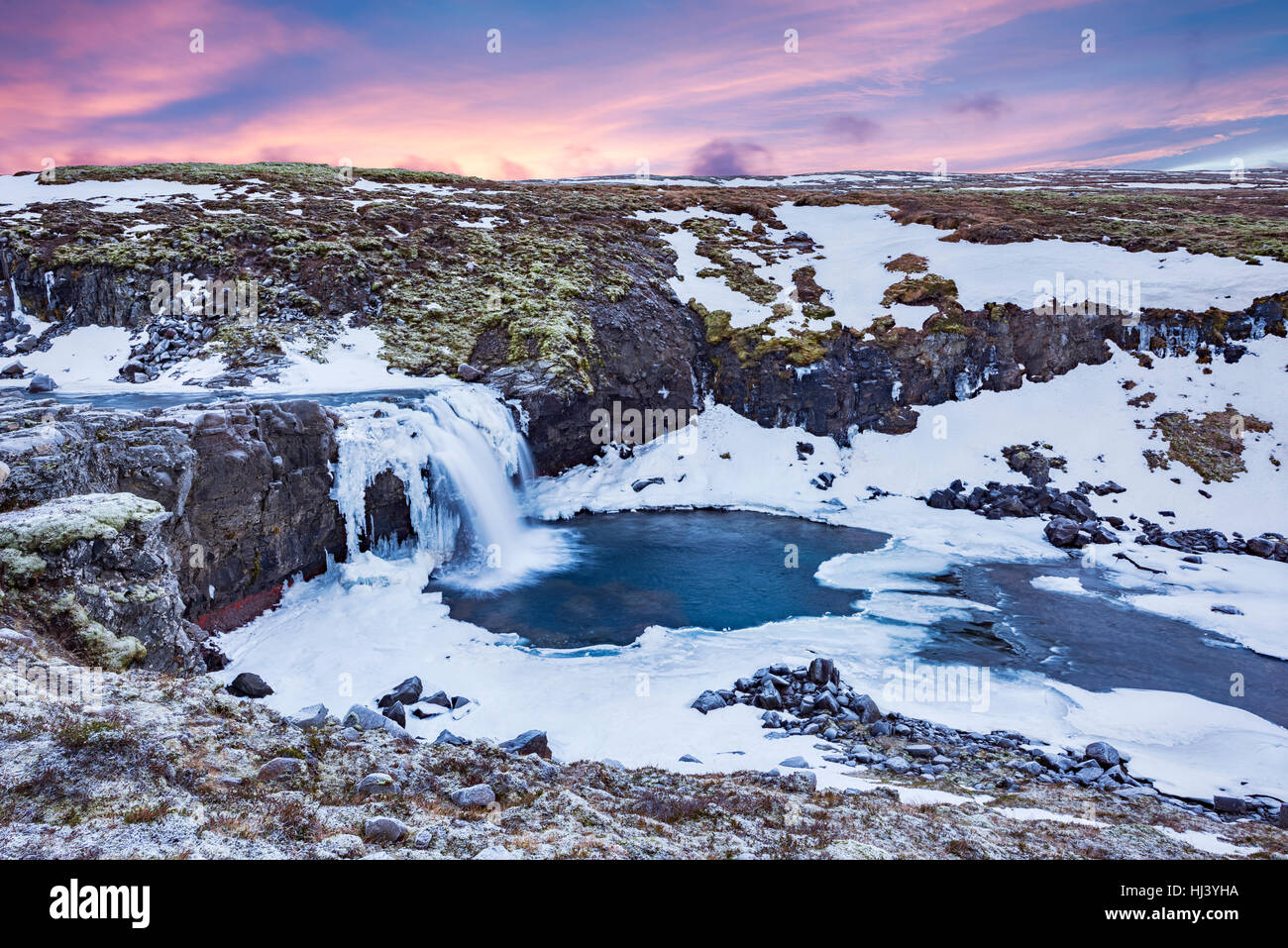 Une cascade de neige froide dans les hautes terres d'Islande encadrée par un ciel pastel et le terrain accidenté offre des paysages pittoresques illustrant le désert gelé Banque D'Images